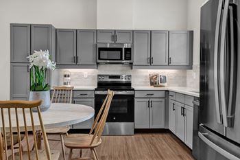 A modern kitchen with a white table and chairs, a vase of white flowers, and stainless steel appliances.